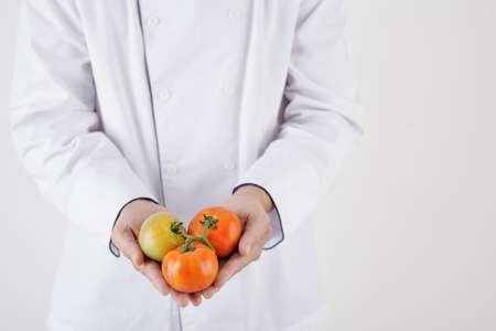 Close-up image of chef in white uniform holding fresh tomatoesの写真素材