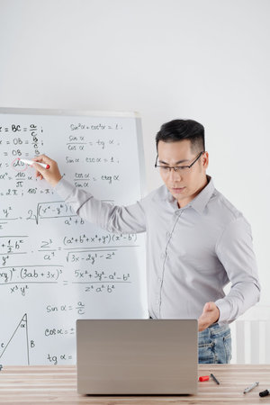 Tutor explaining math topic to student during online class, he is drawing formulas on whiteboardの写真素材