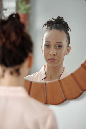 Serious beautiful Black young woman with green eyes looking at mirrorの写真素材