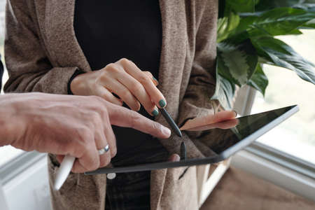 Close-up image of business people pointing at screen of tablet computer when choosing logo for new companyの写真素材