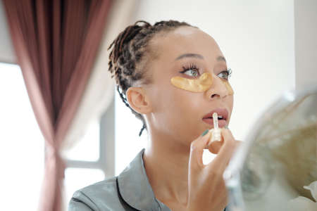 Beautiful woman with undereye patches applying moisturizing lip balm or glossの写真素材