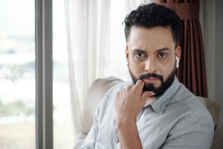 Frowning serious man listening to podcast or audiobook and looking at cameraの写真素材