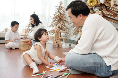Happy father and daughter drawing Christmas pictures on the floorの写真素材