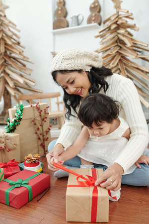 Happy mother and her little daughter opening Christmas presents in the morningの写真素材