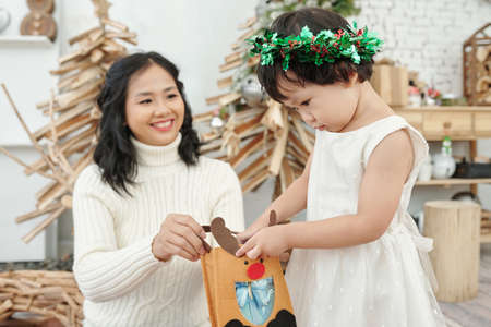 Smiling mother looking at happy curious little girl opening bag with Christmas presentの写真素材