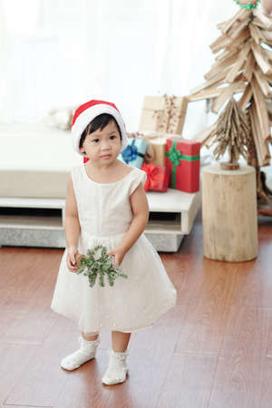 Cute little girl standing on the floor in living room with small Christmas tree at homeの写真素材