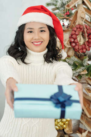 Portrait of smiling woman in Santa hat giving wrapped Christmas giftの写真素材
