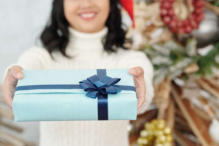 Hands of cheerful woman giving blue New Year present with big bowの写真素材