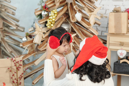 Cute little daughter asking mother to help her with wearing red earmuffsの写真素材