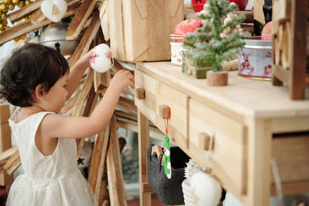 Adorable little girl decorating room with Christmas toys for celebrationの写真素材