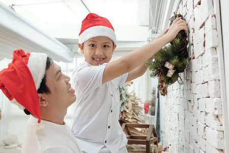 Father lifting preteen son excited to hang handmade wreath on wallの写真素材
