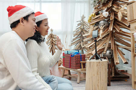 Happy couple in Santa hats videocalling friends and family members to wish merry Christmas and Happy New Yearの写真素材