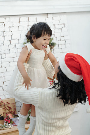 Mother in Santa hat lifting laughing little daughter in white dressの写真素材