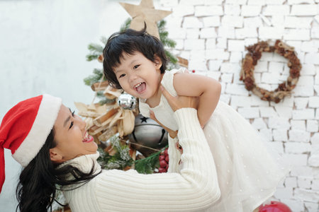 Cheerful mother lifting joyful laughing little daughter when they are celebrating Christmas at homeの写真素材