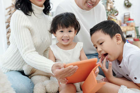 Adorable little girl, her bother and parents watching Christmas movie on tablet computerの写真素材