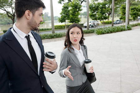 Young businesswoman drinking morning coffee and discussing important meeting with colleague when they are walking outdoorsの写真素材