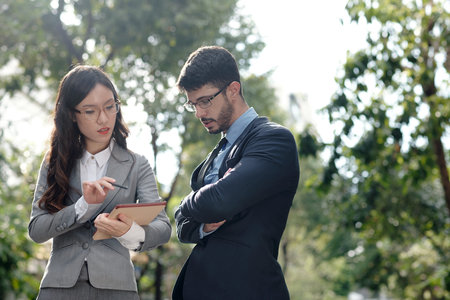 Serious young businesswoman reading document to colleague when they are walking outdoorsの写真素材