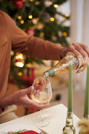 Hands of man filling glass with champagne when enjoying Christmas dinner at homeの写真素材