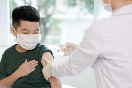 Little boy in medical mask letting doctor to inject vaccine against coronavirusの写真素材