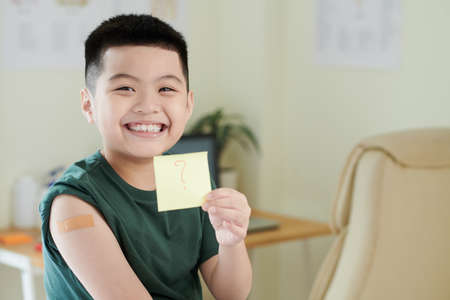 Smiling little boy vaccinated against coronavirus showing sticker with question markの写真素材