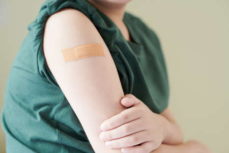 Shoulder of little boy with adhesive plaster over covid-19 vaccine injection siteの写真素材