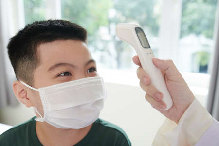 Positive boy getting his body temperature measured before getting vaccine in clinicの写真素材