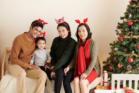 Happy family of child, parents and grandmother sitting on sofa at home next to Christmas tree