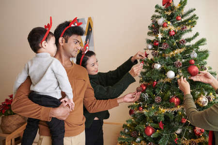 Happy mother, father and little son decorating Christmas tree at home for winter holidaysの写真素材
