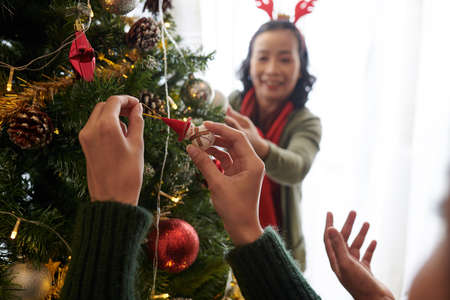 Woman hanging toy on Christmas tree when decorating room with her motherの写真素材