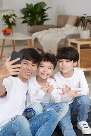 Joyful father taking selfie with two kids at home to post on social media