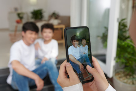 Hands of teenage boy photographing father and his preteen son on smartphoneの写真素材