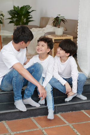 Joyful kids sitting on steps next to their joking father and looking at himの写真素材