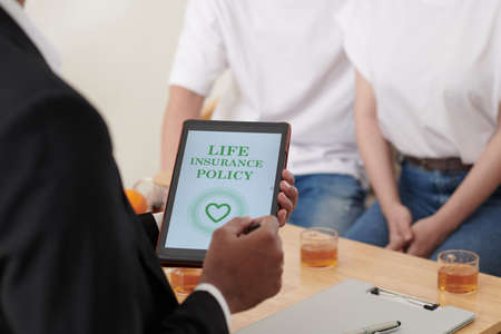 Tablet computer with life insurance policy in hands of agent talking to coupleの写真素材