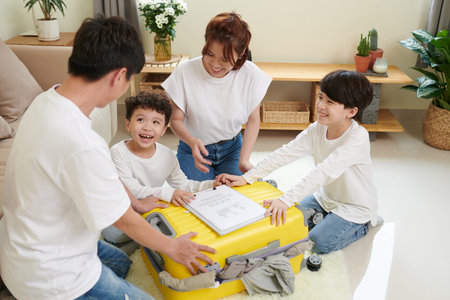Cheerful family of four closing packed suitcase with travel insurance policy document on it