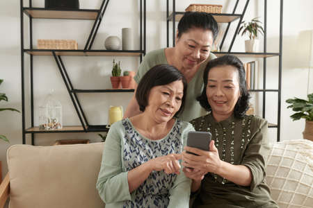 Group of senior female friends discussing and choosing photos to upload on social mediaの写真素材