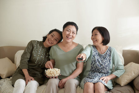 Group of happy senior friends eating popcorn and watching comedy movie on tv at home