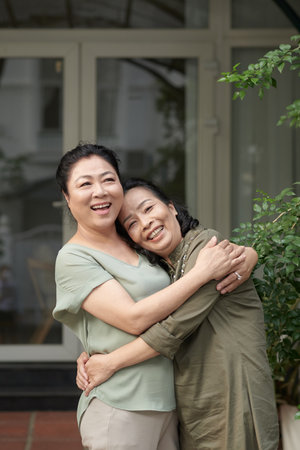 Two senior best friend hugging and looking at camera when standing outdoorsの写真素材