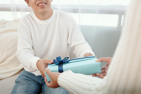Smiling man accepting Christmas present from his wife wrapped in blue wrapping paperの写真素材