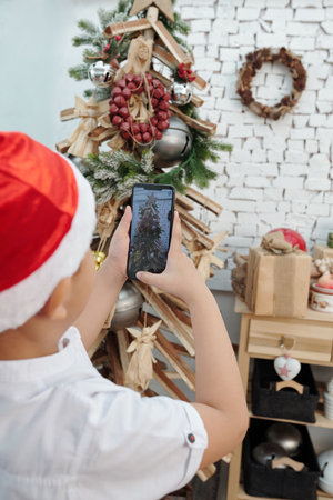 Boy photographing decorated Christmas tree on smartphone to post on social mediaの写真素材