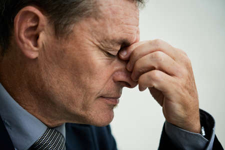 Side view of overworked mature businessman with closed eyes rubbing bridge of nose against isolated backgroundの写真素材