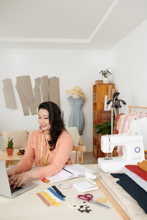 Smiling female tailor working in her studio and answering e-mails from customers