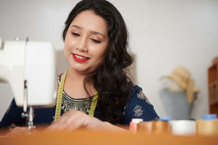 Happy female tailor using sewing machine when making dress for customerの写真素材