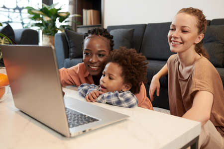 Diverse lesbian couple and little son watching animated cartoon on laptop at homeの写真素材
