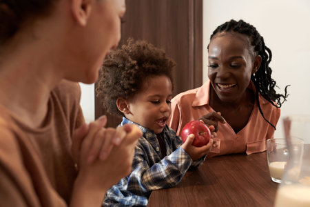 Smilng mother giving red apple to her smiling toddler son after breakfast