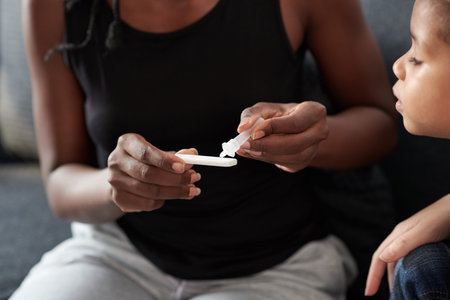 Mother using rapid home-use test kit for saliva, she is transferring three drops of liquid sample to...