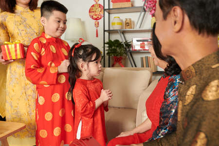 Adorable little girl and her elder brother making traditional gesture when greeting grandparents before Tet dinnerの写真素材