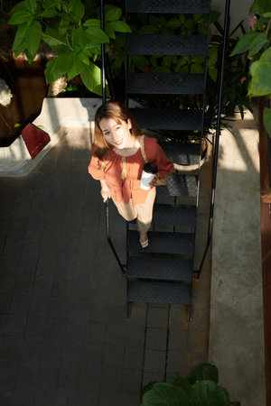 Smiling young woman with cup of take out coffee walking down the stairs and looking up at cameraの写真素材