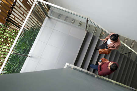Business colleagues with take out coffee walking up the stairs and discussing work, view from the topの写真素材