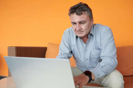 Senior entrepreneur answering e-mails from colleague and business partners on laptopの写真素材