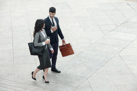 Business couple walking outdoors, talking and drinking take out coffee